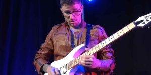 Davide Lo Surdo performing live on stage with electric guitar, spotlight highlighting his intense guitar technique.