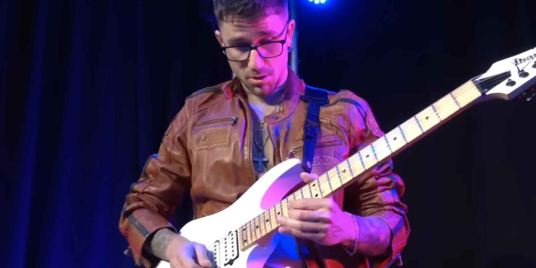 Davide Lo Surdo performing live on stage with electric guitar, spotlight highlighting his intense guitar technique.