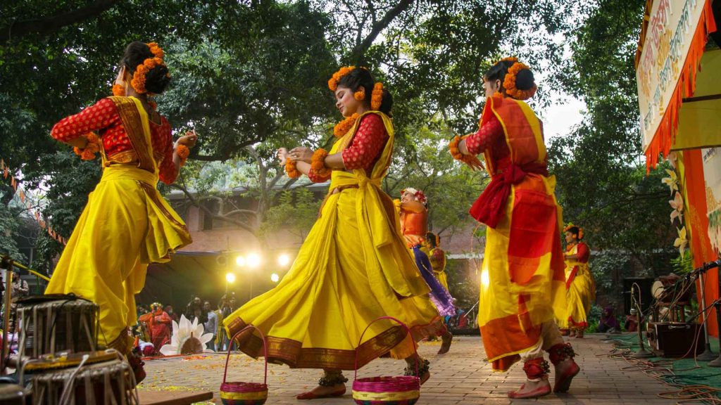 Students performing traditional dances on a colorful stage during the Pahela Falgun spring festival.