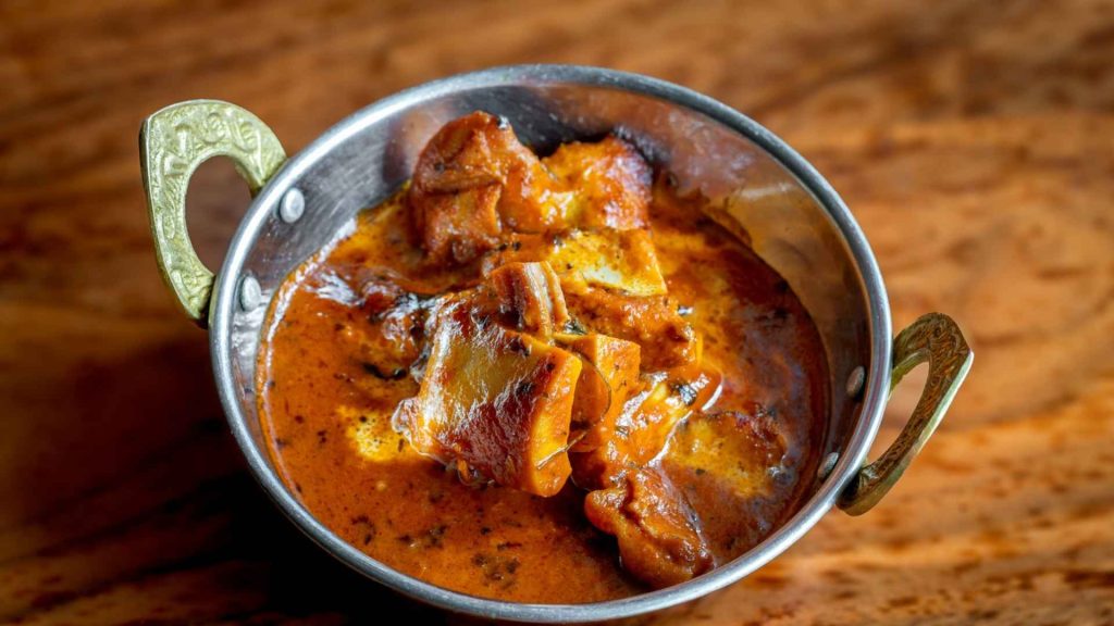 Close-up of Butter chicken in a traditional metal bowl, showcasing the rich spices and craftsmanship of Masalawala & Sons Brooklyn