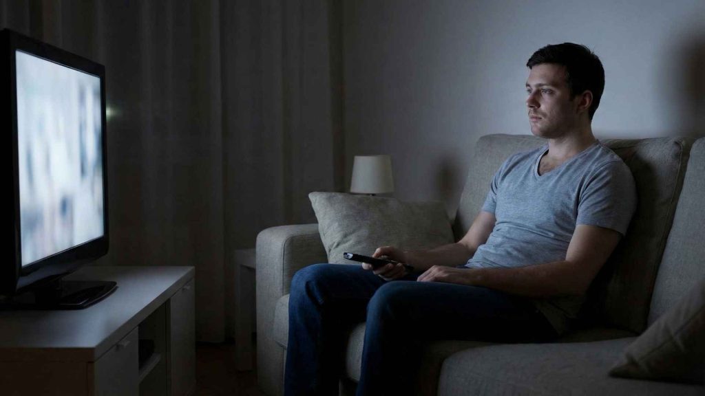Tired man sitting on couch watching television alone