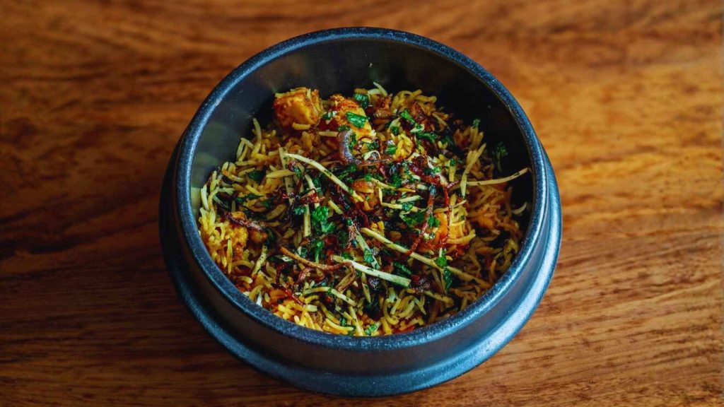 A dark bowl of aromatic Bengali biryani topped with fresh herbs and fried onions at Masalawala & Sons Brooklyn, a staple of the Park Slope food scene