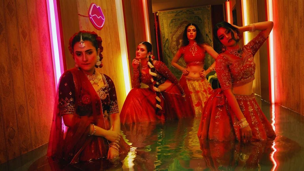 Four women in traditional red and gold lehengas posing in a water-filled hallway for a sequence in the movie Pressure Cooker.