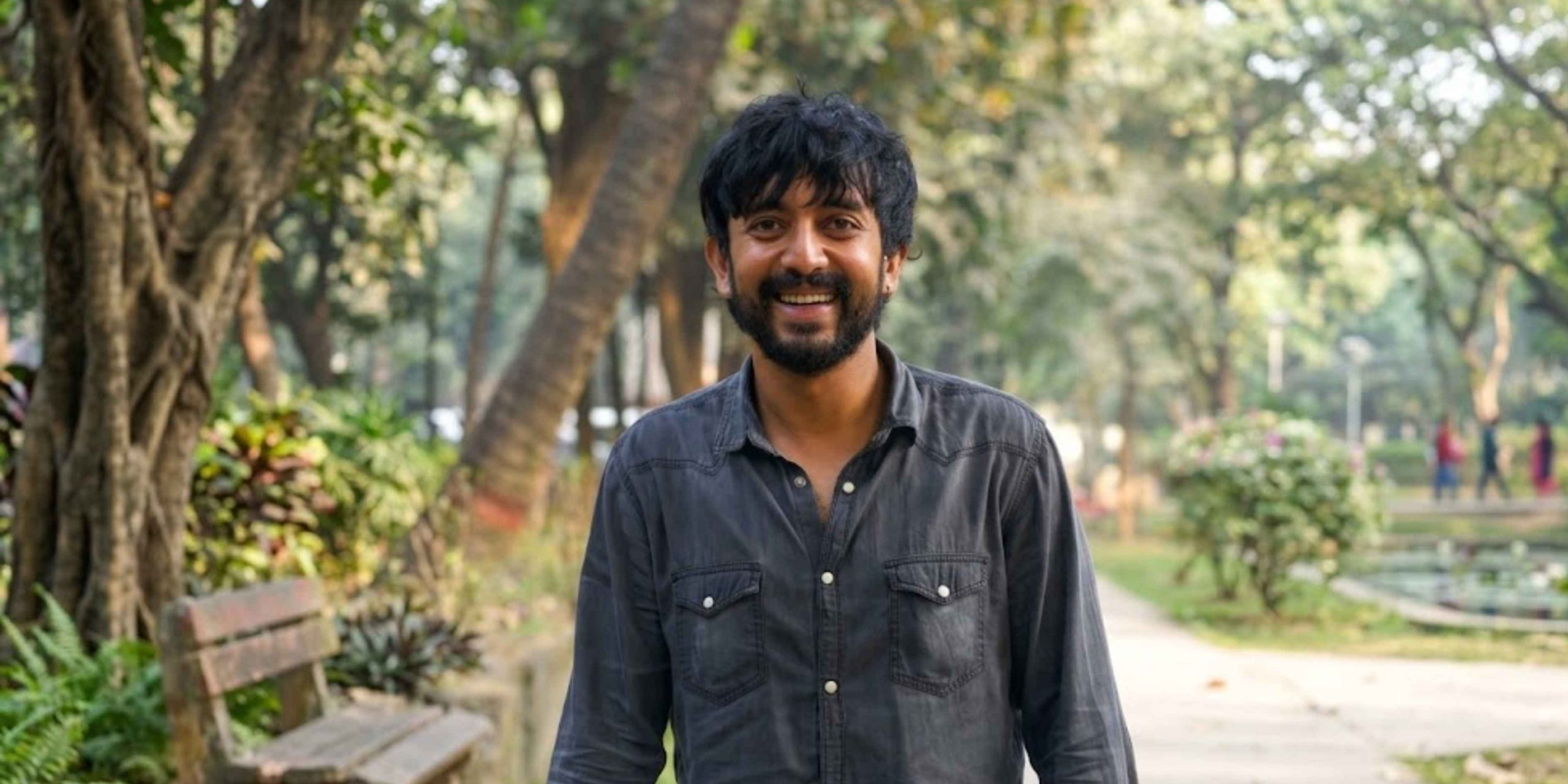 A candid portrait of actor Faizul Yameen smiling in a lush green park setting, reflecting his grounded and approachable personality.