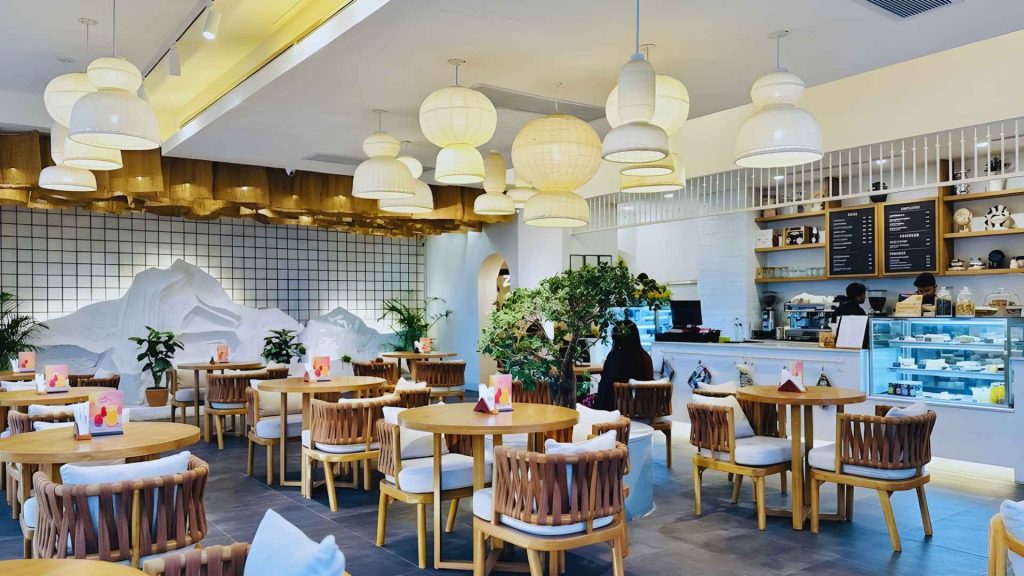 Wide interior shot of Zen Café in Dhanmondi, showcasing unique rope-wrapped chairs, layered pendant lighting, and a stylized mountain wall mural. A popular spot in the Best Café in Dhanmondi discussion.