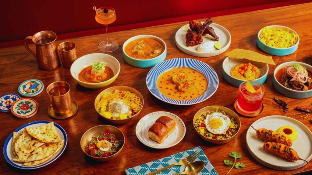 An extensive spread of modern Indian dishes, signature cocktails, and craft appetizers on a wooden table at The Bombay Canteen.