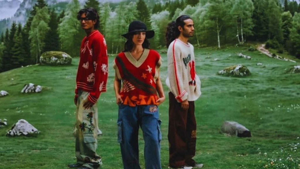 Models wearing Rastah oversized patterned knit sweaters and streetwear trousers in a lush green mountain landscape, highlighting premium South Asian apparel.