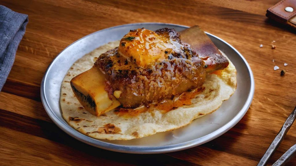 Succulent bone-in meat rib served over a traditional flatbread at Dhamaka, highlighting authentic regional Indian spices.