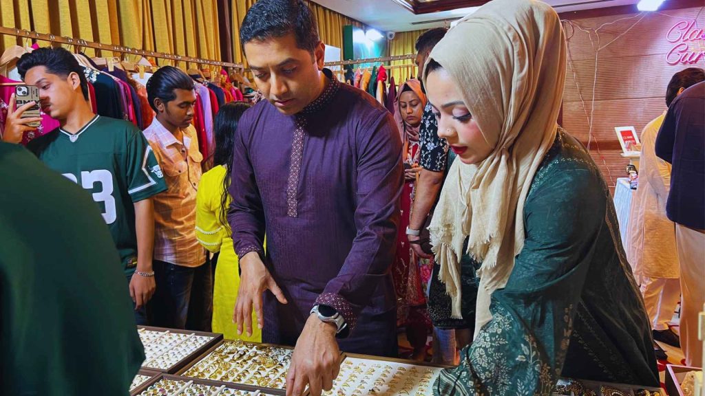 A man and woman examining gold jewelry displays at the Qurbani Eid Exhibition by Glamshow, highlighting luxury fashion and lifestyle products in Dhaka.