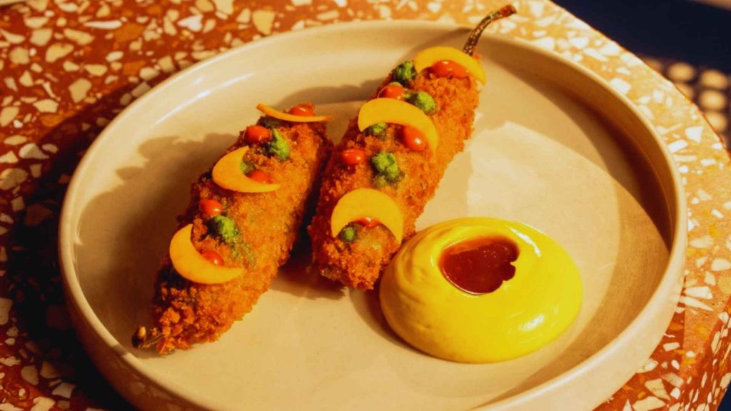 Crispy breaded stuffed chili peppers garnished with vibrant chutneys and served with a creamy dip at The Bombay Canteen.