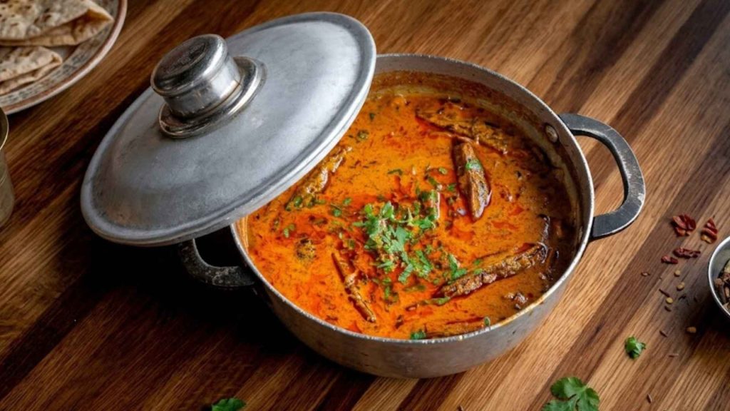 A pot of rich, vibrant orange Indian curry garnished with fresh cilantro from the kitchen of Dhamaka.