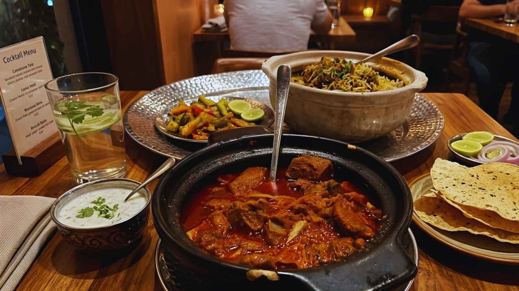 A diverse spread of Indian dishes including Biryani, meat curry, and papadum at Dhamaka NYC.
